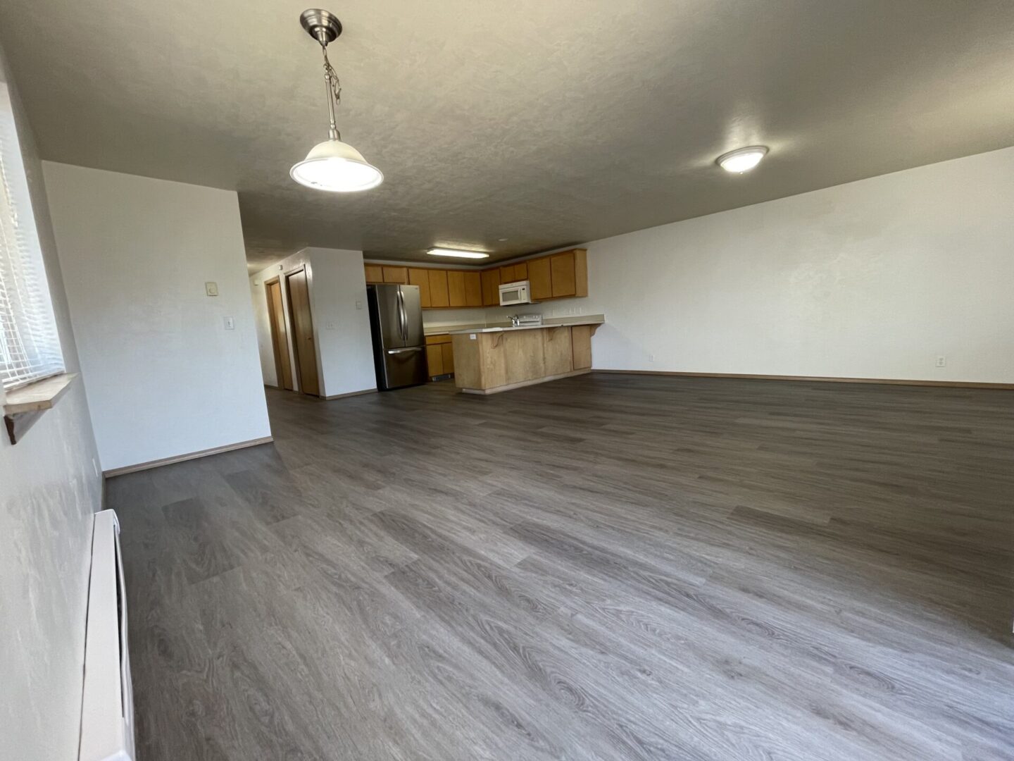 Spacious empty room with modern flooring and kitchen area.