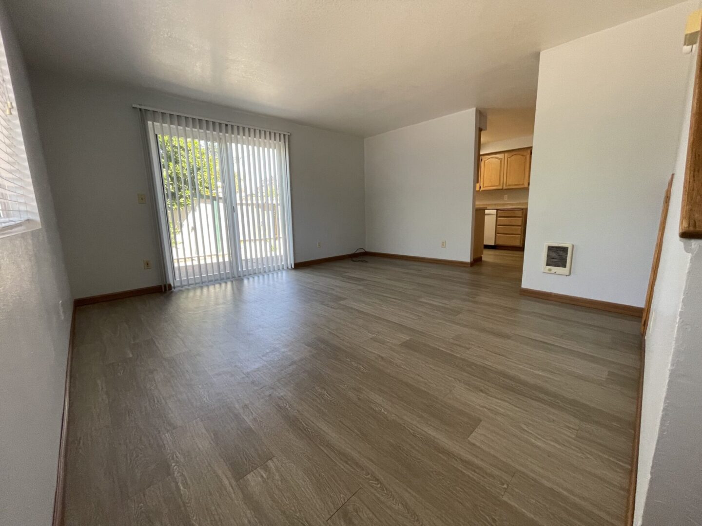 Empty room with wooden flooring and sliding glass door.