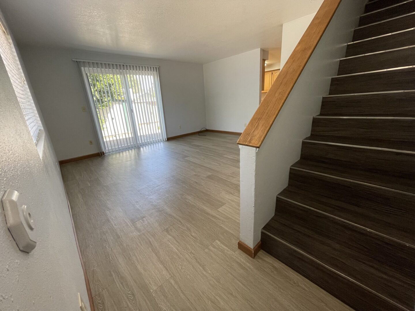 Bright empty room with wooden flooring and staircase.
