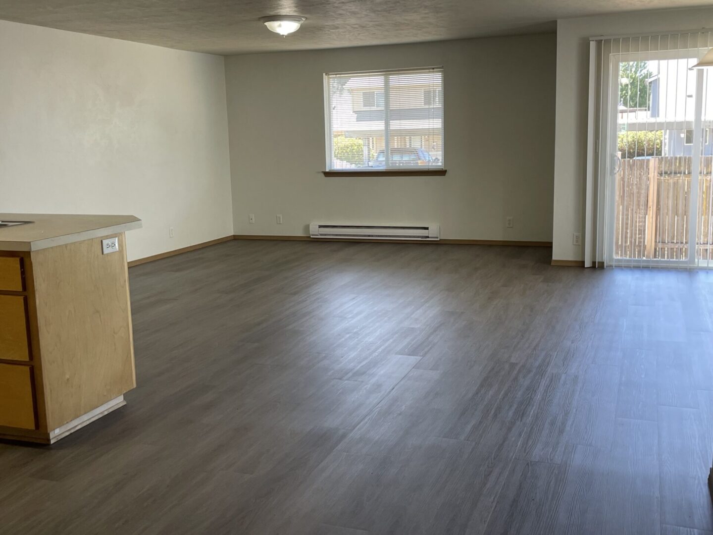 Empty living room with large window and wood flooring.